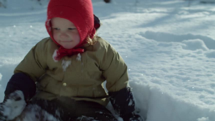 A child walks then sits in the snow