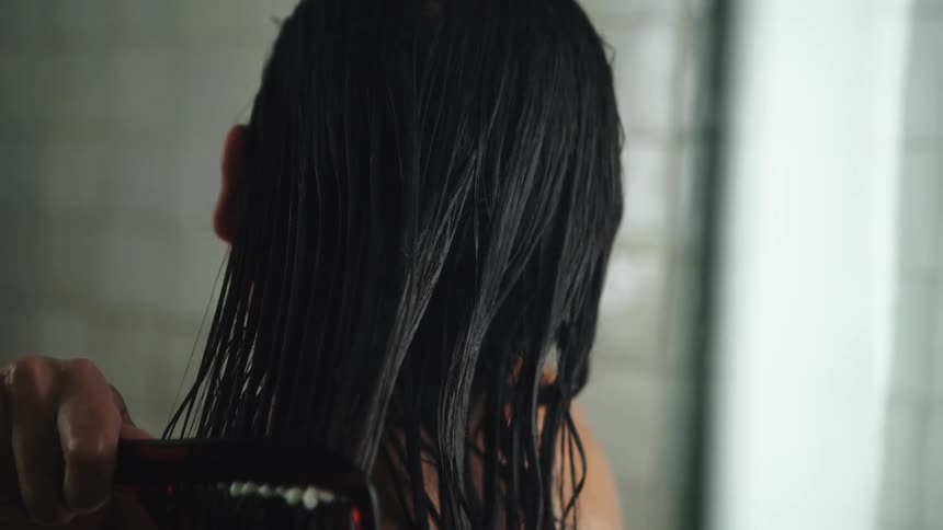 A woman uses a wide tooth comb on her wet hair in the shower