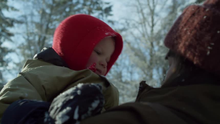 A woman picks up her son in the snow and laughs when he hits her in the face