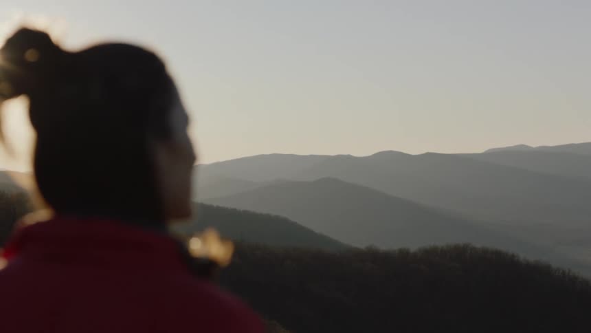 Woman looks out over mountain view on a windy, sunny day