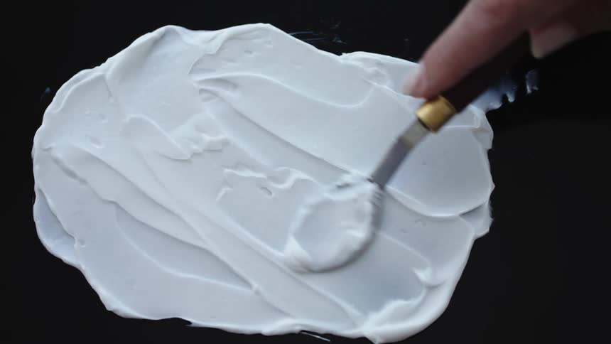 A person spreads white cream across a glass table