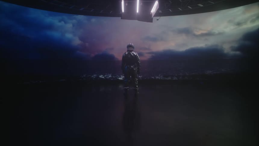 A person in a space suit stands looking out while a light from above glows brighter