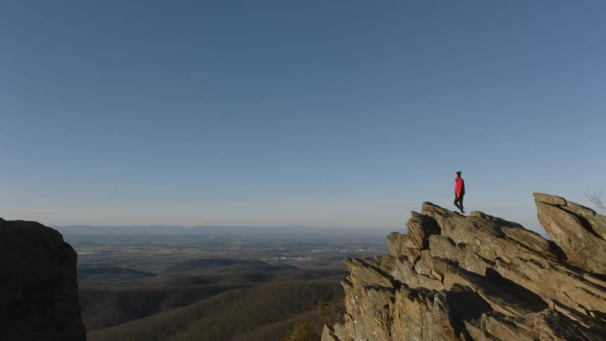 A woman looks out from a rock formation over rolling hills