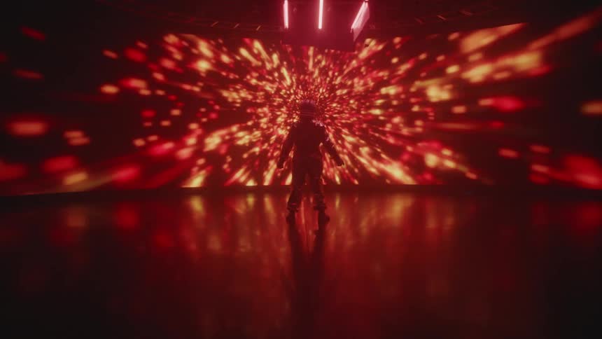 A person wears a helmet and full costume while standing in front of a screen displaying laser graphics