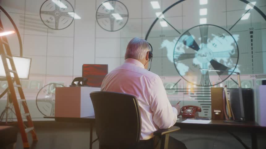 A man spins in his desk chair and changes the screen behind him from graphs to a global map