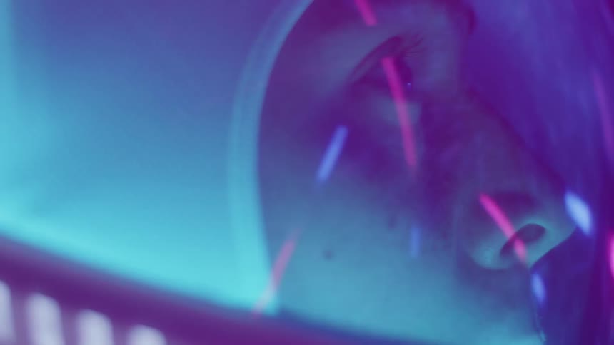 Person wearing astronaut helmet stares as light show reflects off glass front