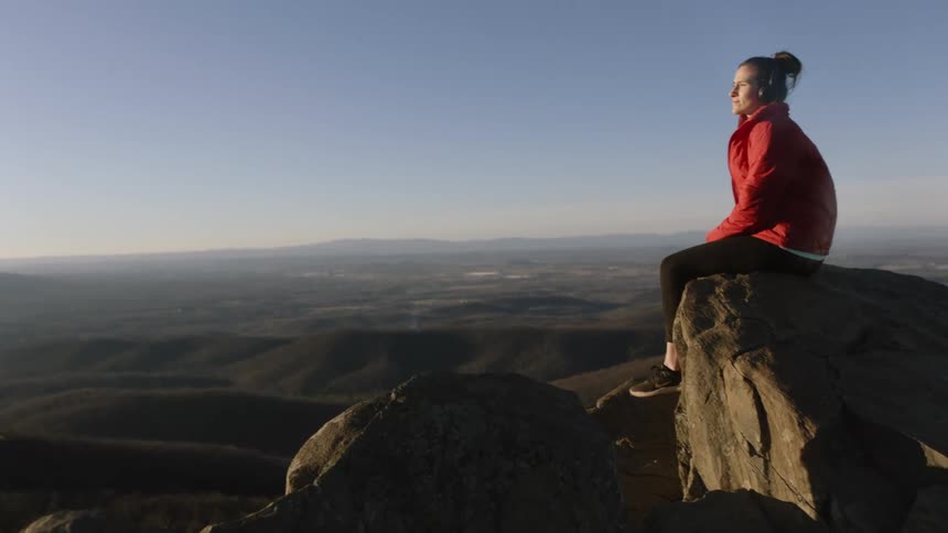 A woman sits on a mountain ledge listening to music
