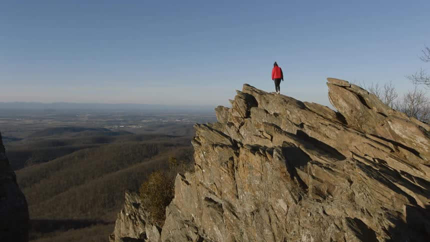A woman hikes up a mountain rock formation over scenic view