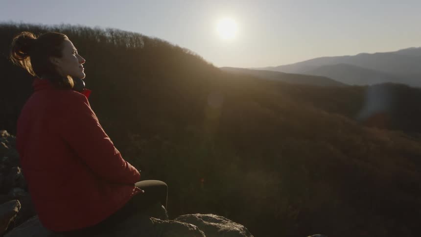 A woman sits on a mountain top and takes off her headphones