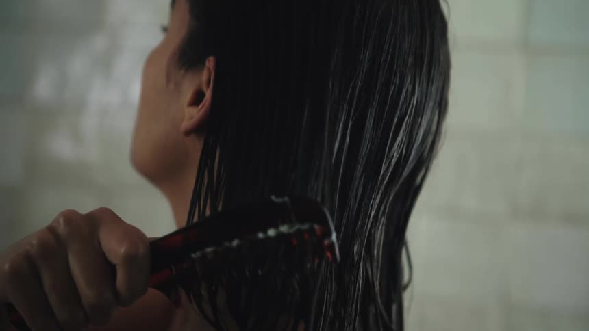 Woman distributes mixture through her hair using a comb while standing in bathroom