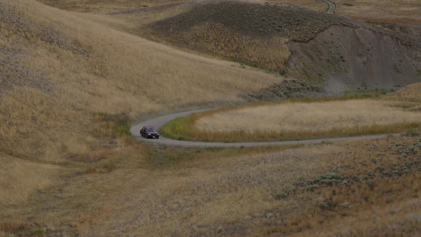 An automobile travels around a bend on a road surrounded by mountains