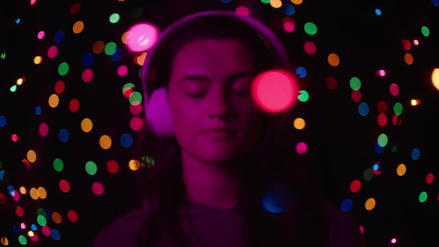 A woman wearing headphones closes her eyes as the lights go down and colorful lights begin to orbit around her