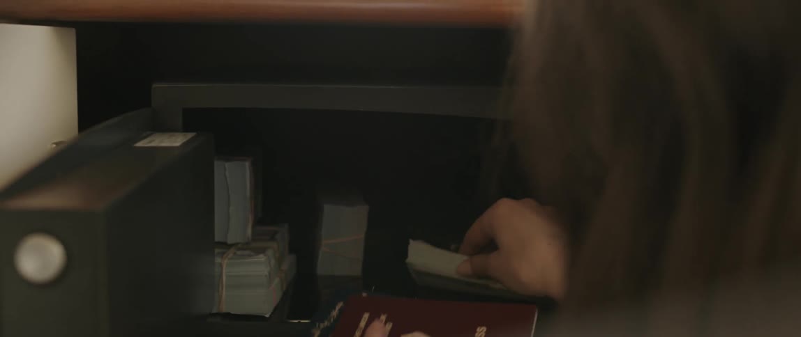 A woman rummages through a safe and pulls out passports and cash
