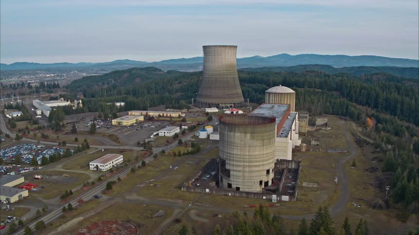 The reactors and buildings of a shut down nuclear power plant surrounded by trees and hills