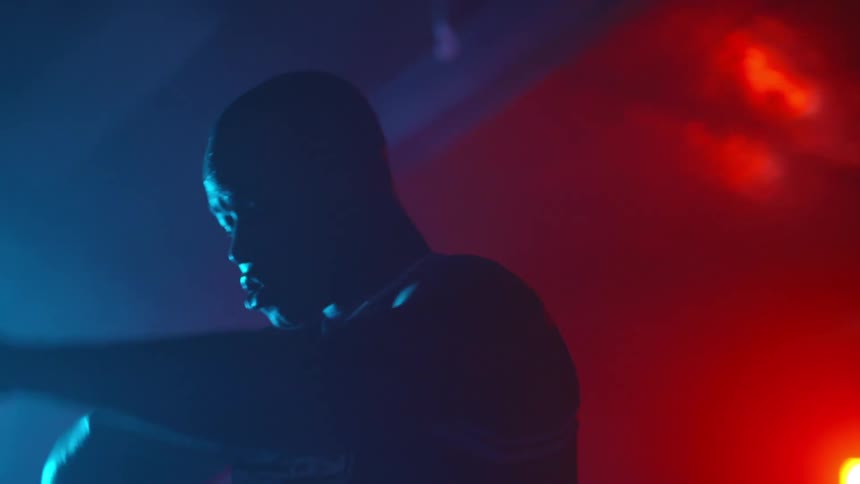 Silhouette of a man standing inside a dimly lit gym stretching under colorful lights