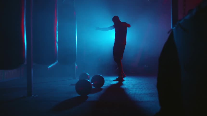 Silhouette of a man standing inside a dimly lit gym stretching