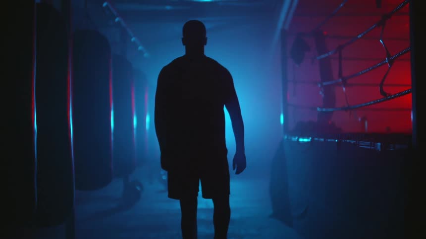 A man is walking through a gym that has a boxing ring