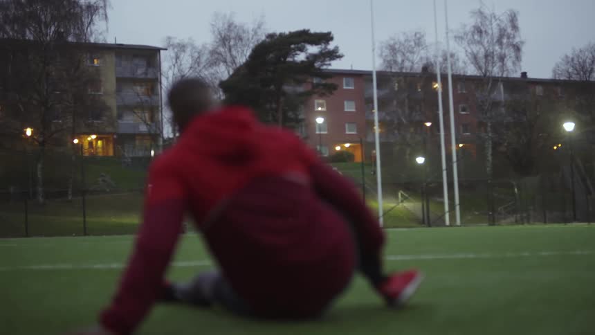 A man sitting on the field turf stretching out his legs before a workout