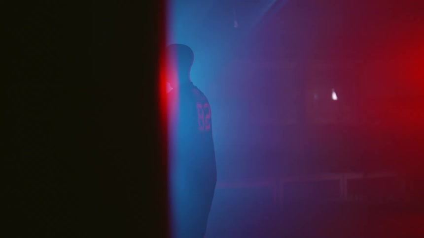 A man is jogging and walking in a dark room with blue and red lights