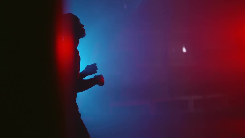 Silhouette of a man inside a dimly lit gym sparring alone