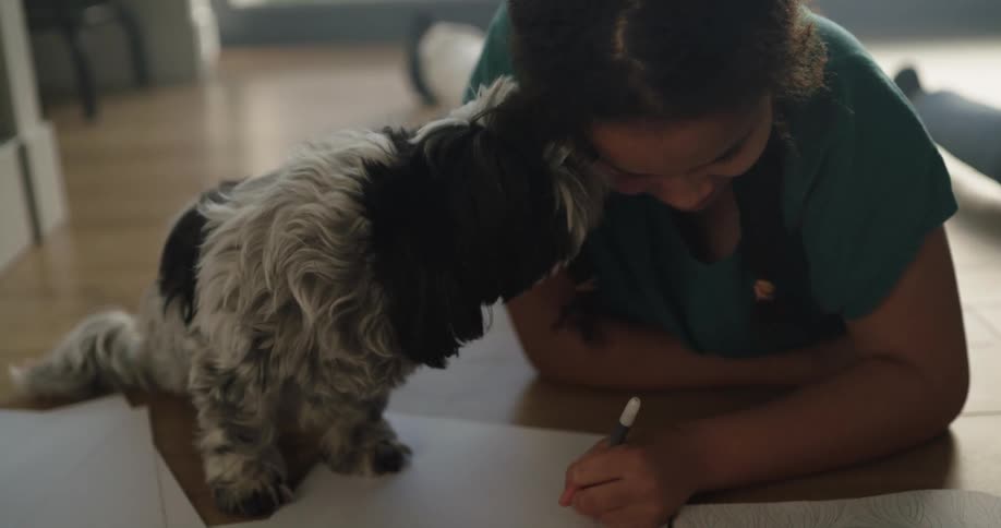 A child trying to draw while a dog licks her face