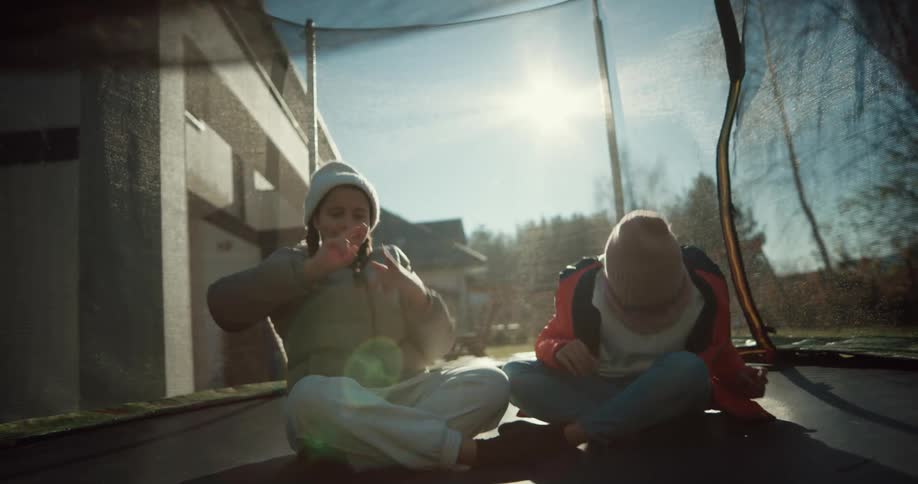 Two girls are bouncing as they sit on a trampoline