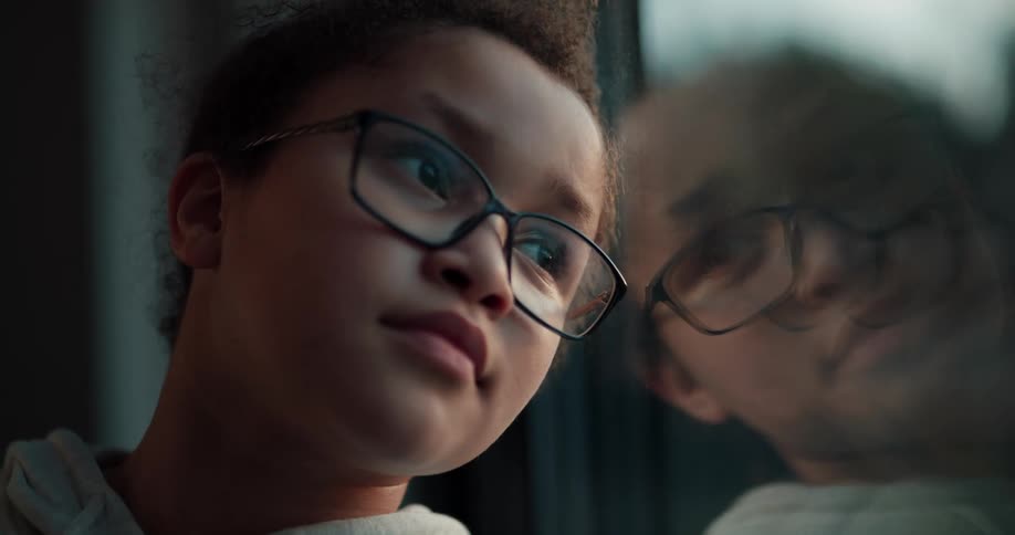 A girl sits with her head propped against a window as she looks outside