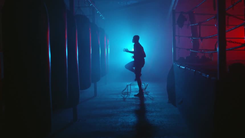 A man is running in place next to a boxing ring at a gym