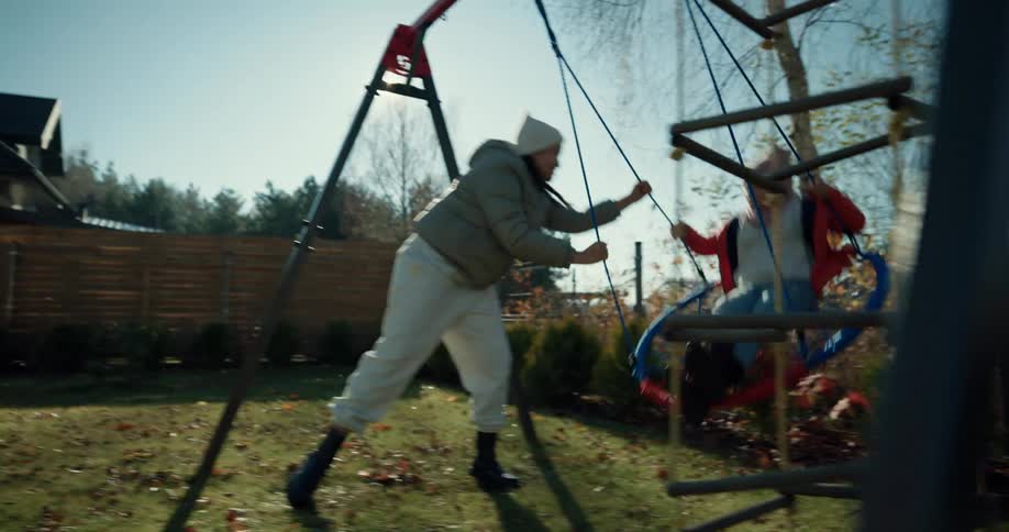 A little girl is pushed on the backyard swing set by her big sister