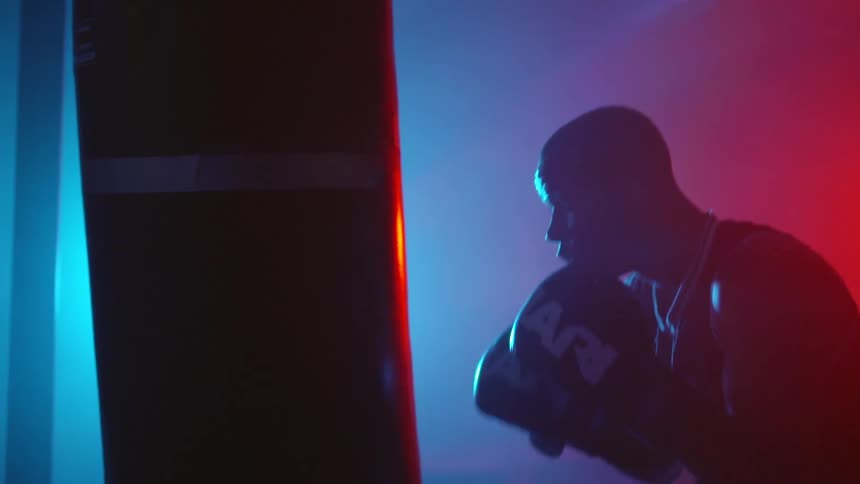 A man trains by striking a punching bag in a dimly lit boxing gym during the day