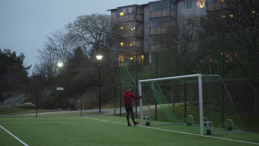 A man walking on a soccer field grabs the goal and holds onto it