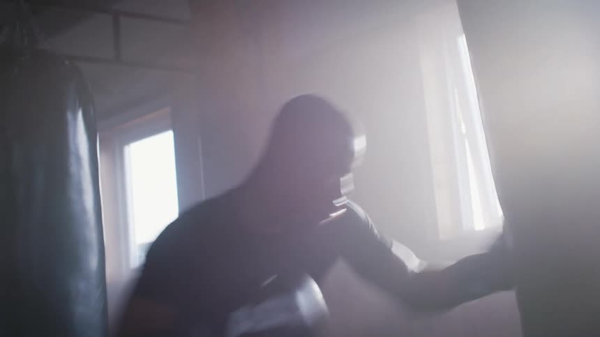 A boxer trains by striking a punching bag in a boxing gym during the day
