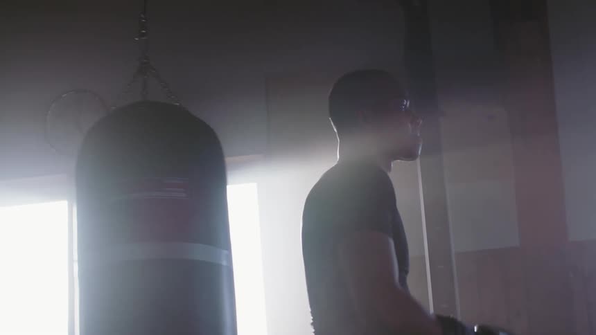 A man with boxing gloves on punches his hand as he walks past a punching bag