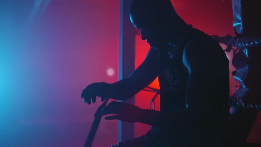 A man wraps his hands while sitting against the ring in a dimly lit boxing gym
