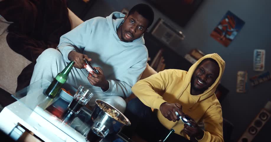 Two men sitting on a couch playing video games laughing and smiling