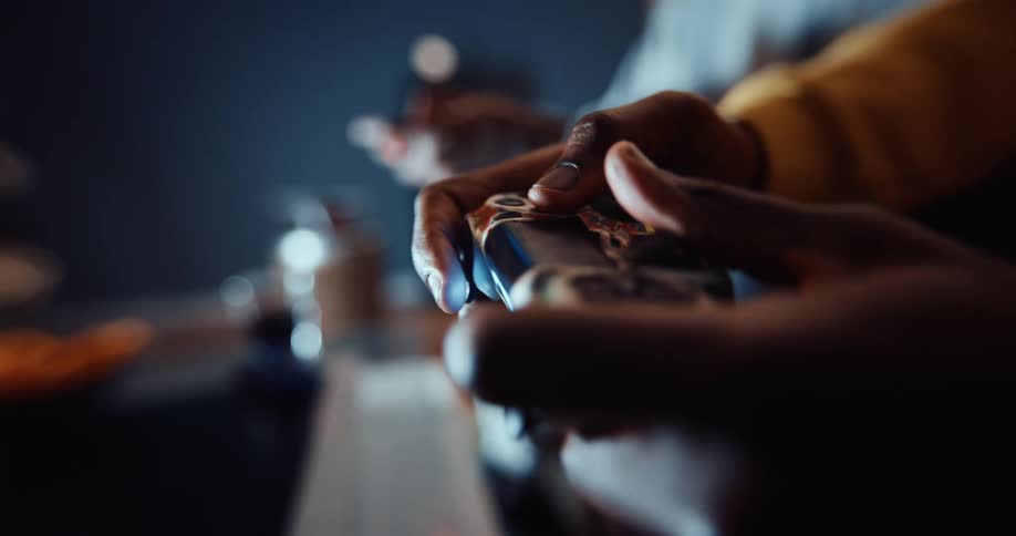 A person presses buttons on a game controller while playing video games with another person in the living room of a house