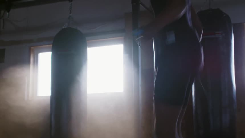 Strong young shirtless man energetically jumping rope inside a dimly lit room
