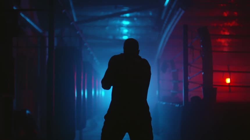 Silhouette of a man practicing boxing moves in a dark room with red and blue lights