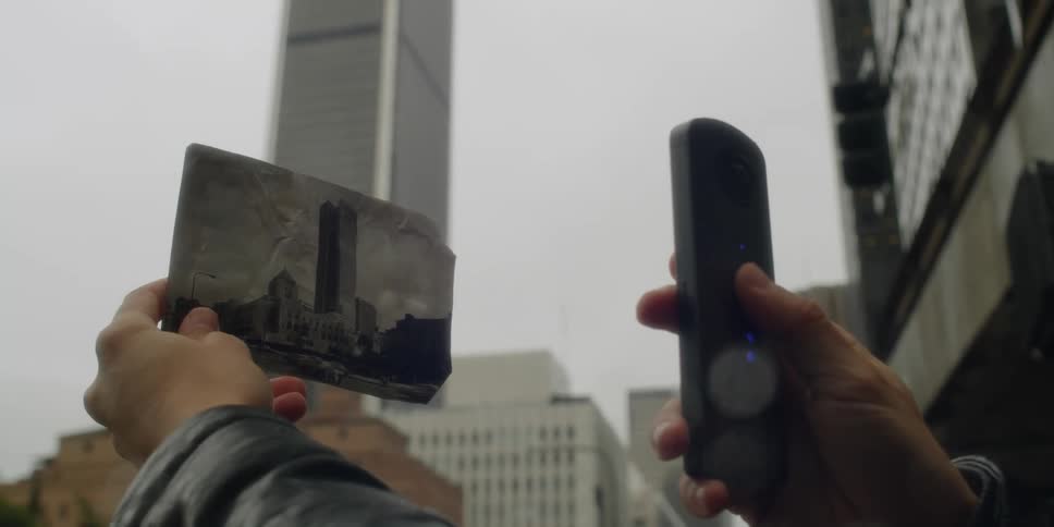 A person uses a smartphone to take a picture of a vintage photograph of a building in the city