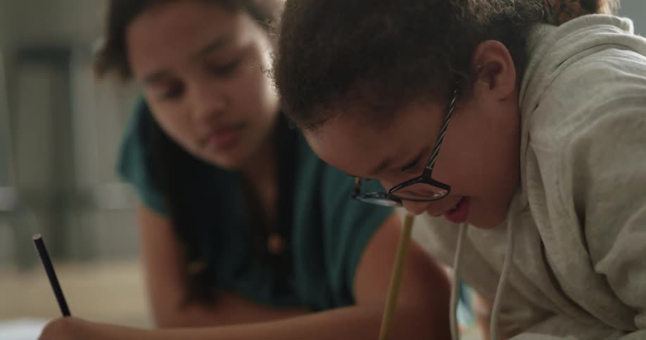 Two girls sit on the floor doing homework at home