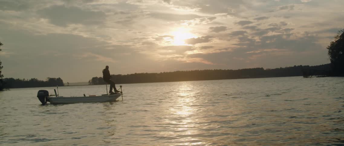 A man is sitting in a fishing boat on a lake on acloudy day