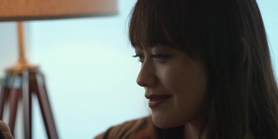 Woman with brown bangs smiles as she uses a smartphone