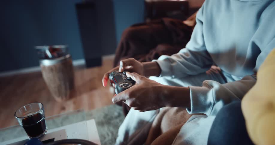 A pair of people play video games together while sitting side by side on a sofa in the living room of a house