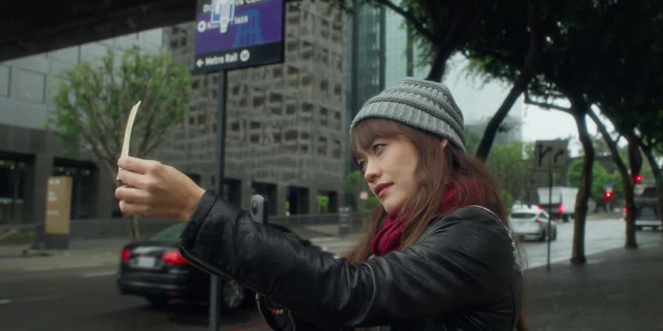 Woman stands near city street comparing view to photograph and smartphone