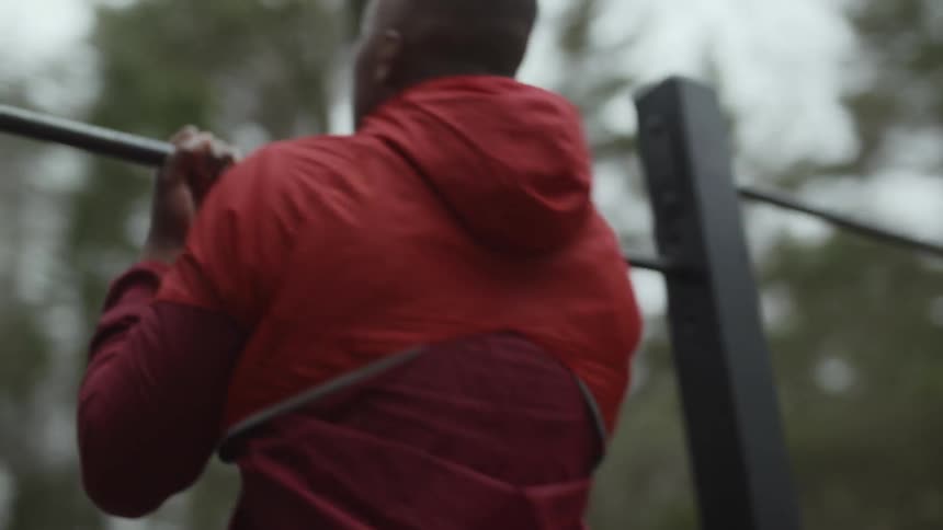 A man is outside in a park doing chin ups on a metal bar