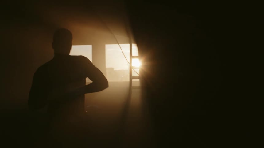 A man paces while putting on boxing gloves in a dark boxing gym