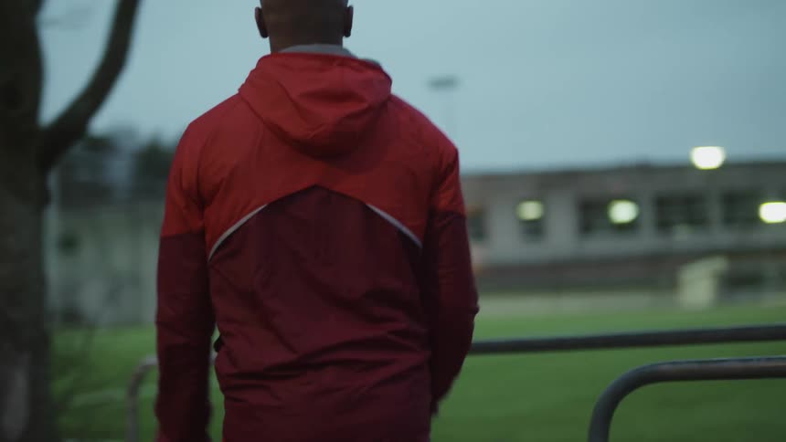 Man wearing a red jacket jogging on a park in the city at morning