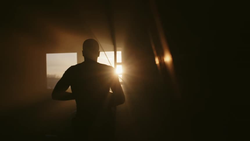The silhouette of a man bending to pick something up and walking away