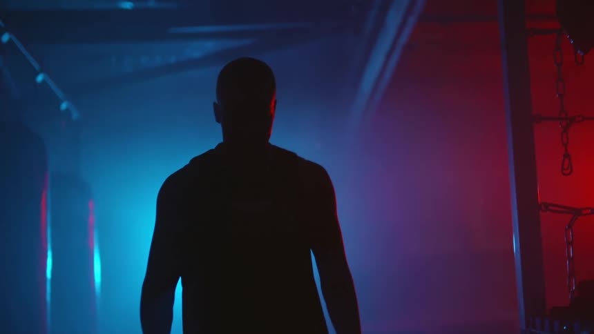 Silhouette of a man walking down a dimly lit hallway inside a gym