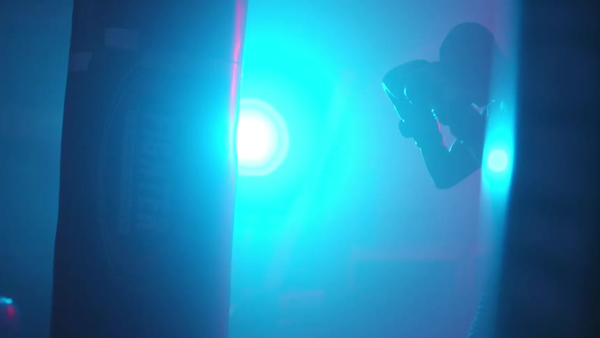 Silhouette of a man inside a dimly lit gym sparring alone